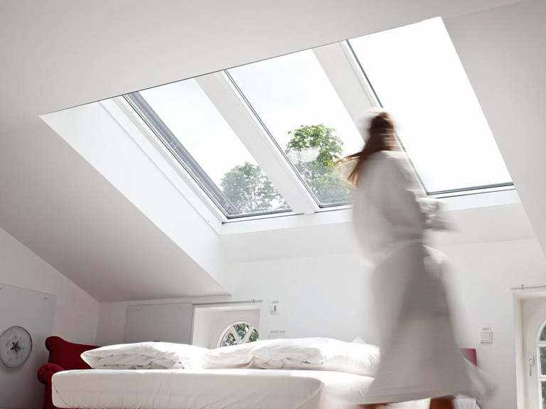 Blurred woman in bathrobe walking through a bright bedroom with large panoramic skylight