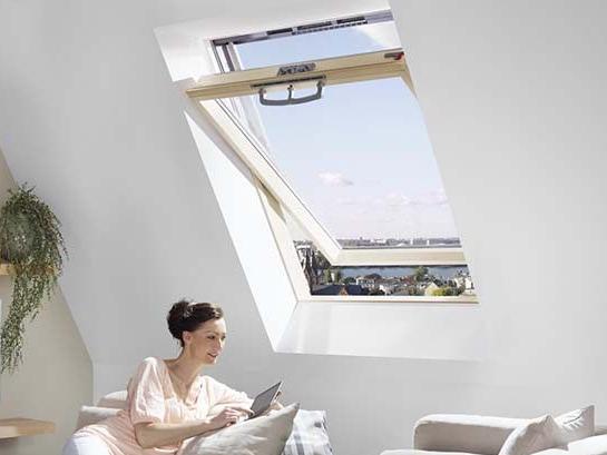 A woman sits in the won room under a RotoQ swinging window and holds a tablet