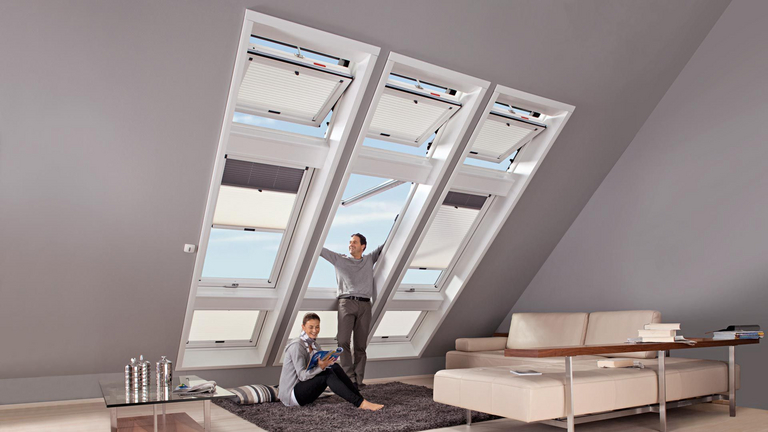 A man looks out an open skylight, a woman sits next to him.